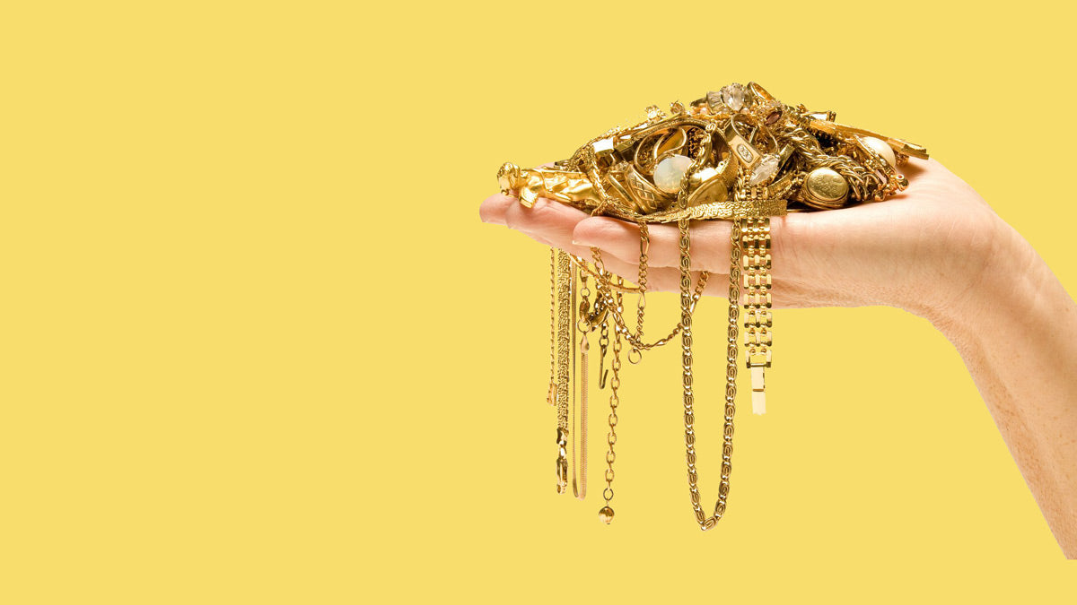 Hand holding gold jewelry against a yellow background. Gold Buyers Examples